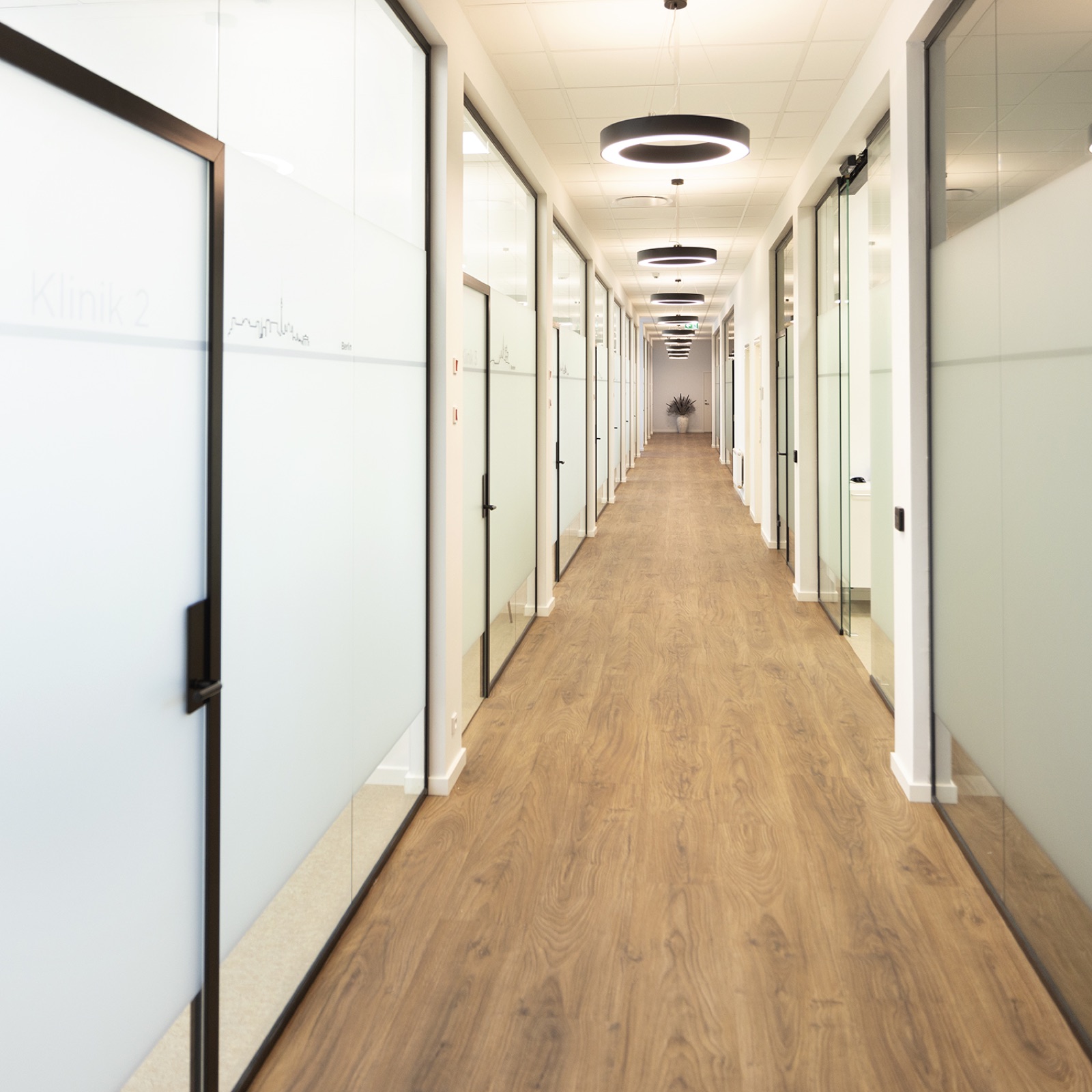 Lys klinikkgang med glassdører til behandlingsrom.